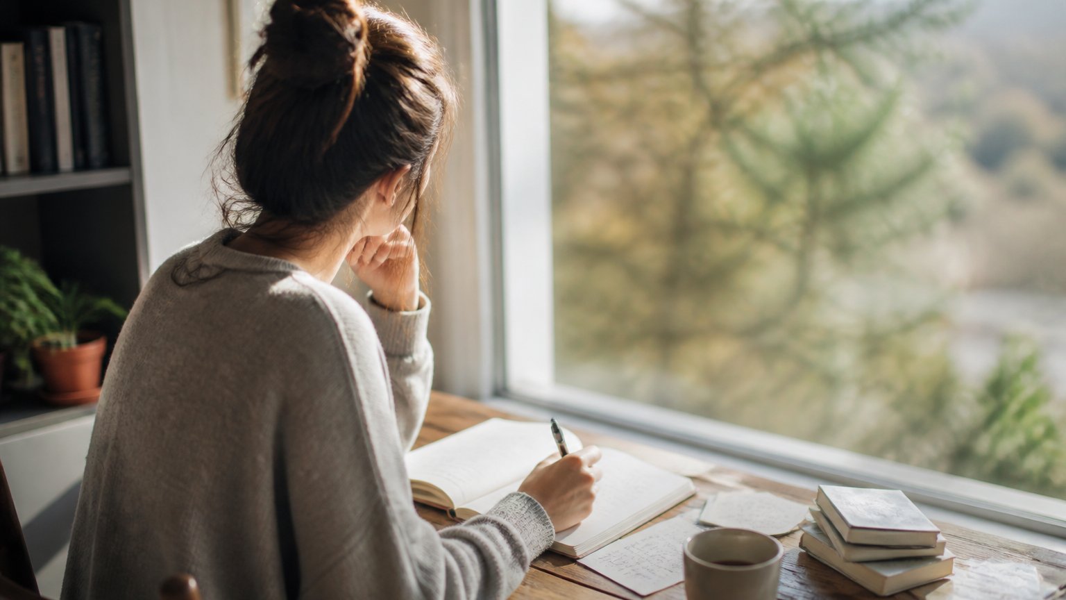 A person journaling by a bright window in soft light during a quiet moment of self-reflection