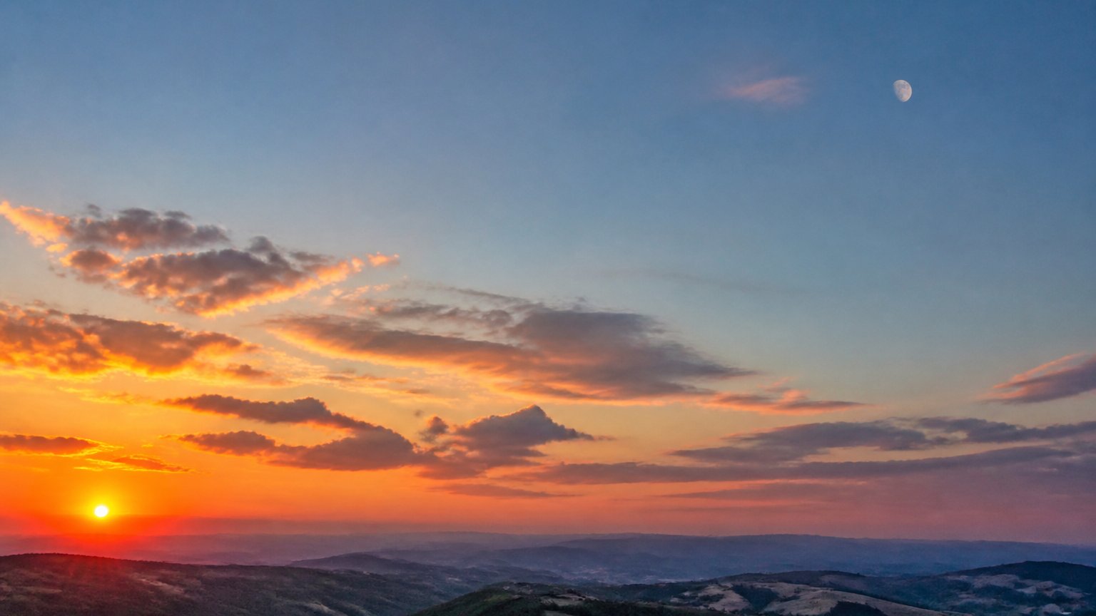 The sun, moon, and horizon rendered symbolically in a warm evening sky